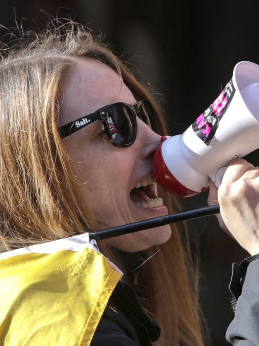Eine Frau schreit in ein Mikrofon auf dem ein Sticker mit der Aufschrift #kandelistüberall zu sehen ist.