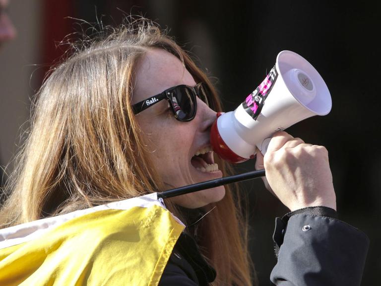 Eine Frau schreit in ein Mikrofon auf dem ein Sticker mit der Aufschrift #kandelistüberall zu sehen ist.