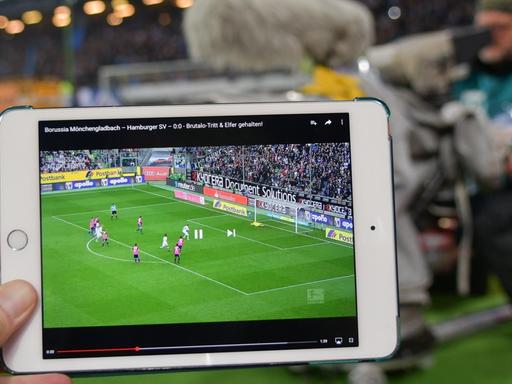 ILLUSTRATION - Der Screenshot eines Fußball-Bundesligaspiels ist am 21.10.2016 in Hamburg im Volksparkstadion auf dem Monitor eines iPad zu sehen. Im Hintergund sitzt ein Kamermannann des Pay-TV-Senders Sky.