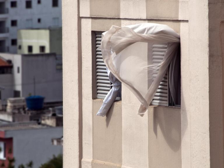 Ein Vorhang weht aus einem offenem Fenster.