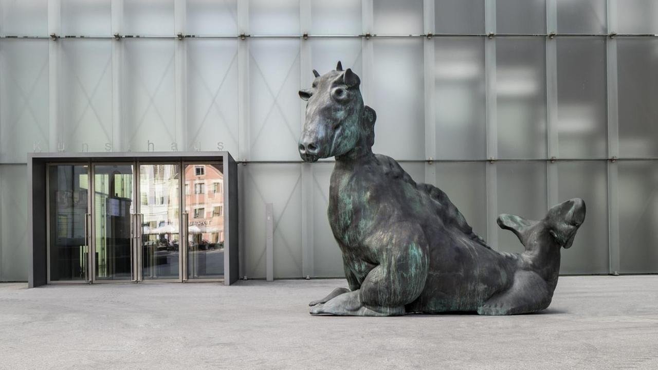 Zu sehen ist Thomas Schüttes Skulptur "Drittes Tier" vor der Fassade des Bregenzer Kunsthauses: ein grünlich patiniertes, über drei Meter hohes Fabelwesen aus Bronze. Zu sehen ist Thomas Schüttes Skulptur "Drittes Tier" vor der Fassade des Bregenzer Kunsthauses: ein grünlich patiniertes, über drei Meter hohes Fabelwesen aus Bronze.