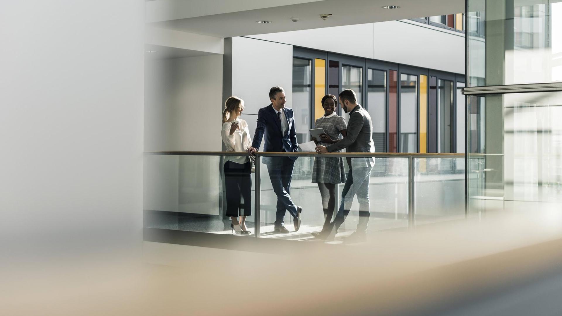 Zwei Frauen und zwei Männer unterhalten sich auf dem Flur eines Bürogebäudes. Zwei Frauen und zwei Männer unterhalten sich auf dem Flur eines Bürogebäudes.