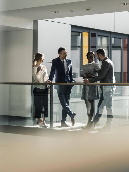 Zwei Frauen und zwei Männer unterhalten sich auf dem Flur eines Bürogebäudes.