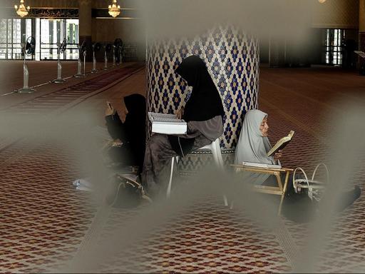 Drei verschleierte Frauen sitzen in einer Moschee gegen eine Säule gelehnt und lesen den Koran.