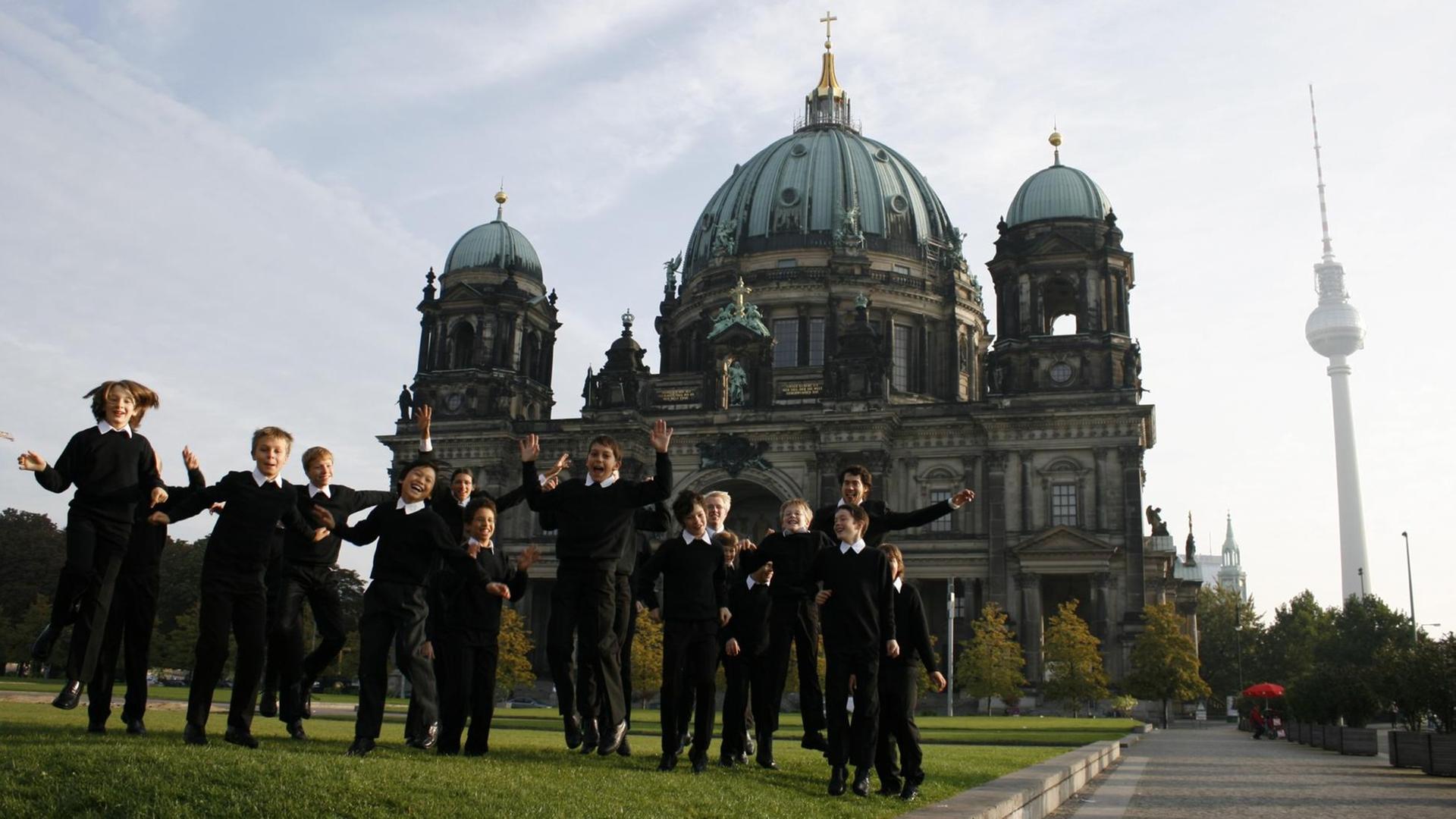 Etliche Jungs in dunkler Chorkleidung toben auf einer Wiese vor dem Berliner Dom. Etliche Jungs in dunkler Chorkleidung toben auf einer Wiese vor dem Berliner Dom.