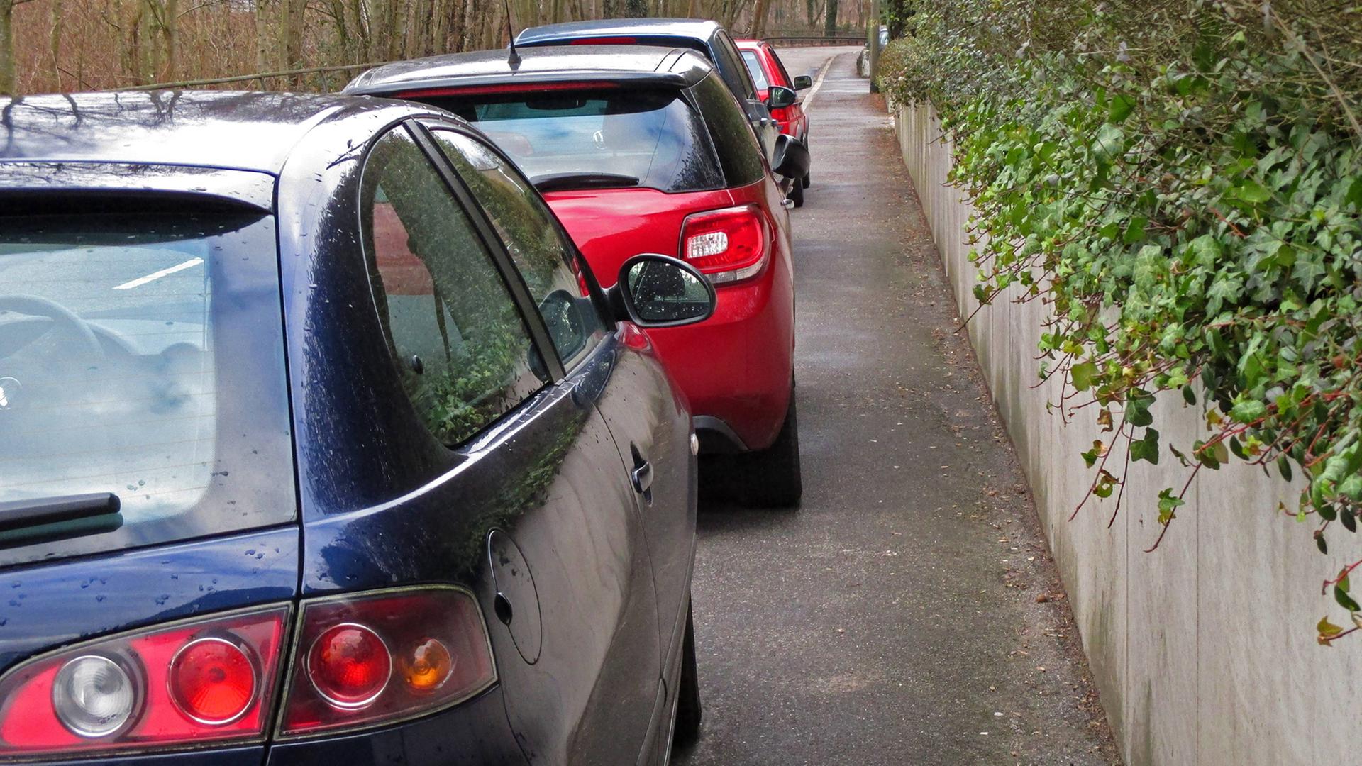 Autos parken so weit auf einem Gehweg, dass Fußgänger nicht an ihnen vorbeigehen können. Autos parken so weit auf einem Gehweg, dass Fußgänger nicht an ihnen vorbeigehen können.