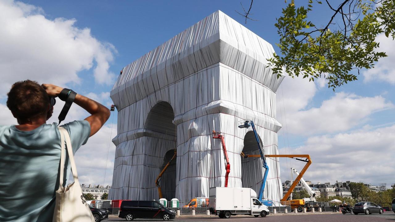 Der Triumphbogen in Paris wird eingepackt. Zu sehen sind Kräne und ein Fotograf. Der Triumphbogen in Paris wird eingepackt. Zu sehen sind Kräne und ein Fotograf.