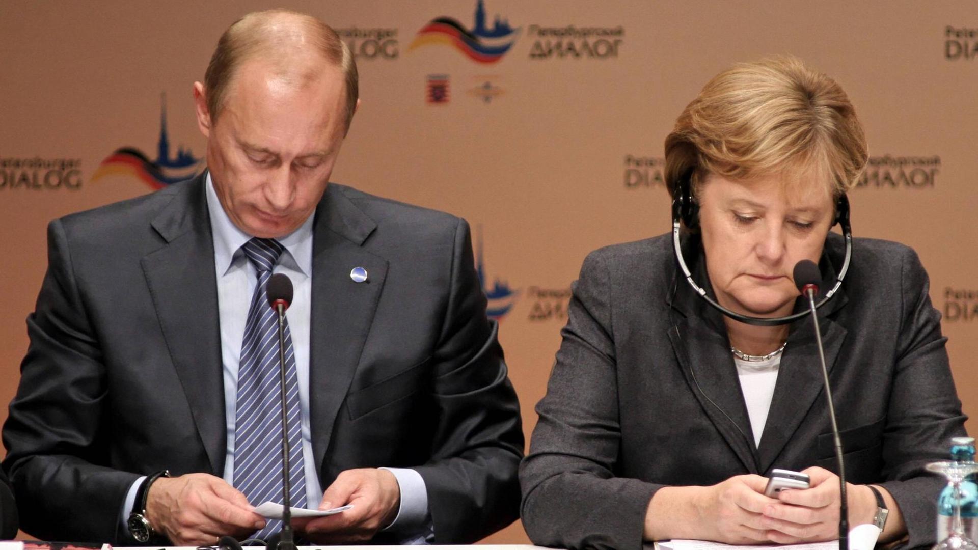 Russlands Präsident Putin und Bundeskanzlerin Merkel bei einer Pressekonferenz anlässlich des Petersburger Dialogs im Jahr 2007. Merkel schaut auf ihr Handy, Putin auf einen Zettel.