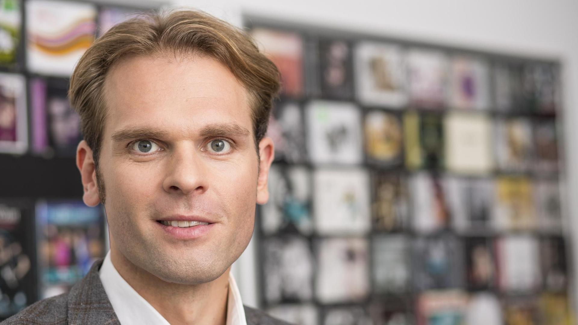 Florian Drücke, Geschäftsführer vom Bundesverband Musikindustrie e.V. vor einem unscharfen Regal voller Tonträger.