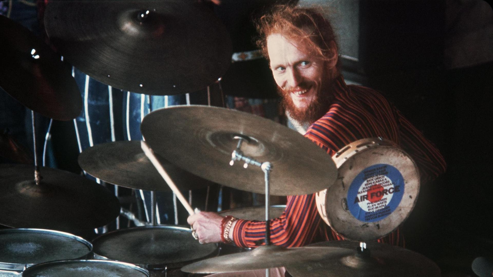 Ginger Baker sitzt am Schlagzeug und grinst. Ginger Baker sitzt am Schlagzeug und grinst.