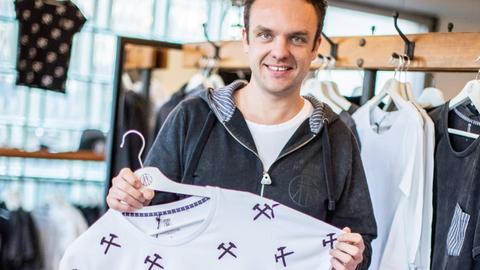 Der Gründer des Labels "Grubenhelden", Matthias Bohm, steht mit einem T-Shirt mit Schlägel- und Eisen-Symbolen in seinem Geschäft in Gladbeck.