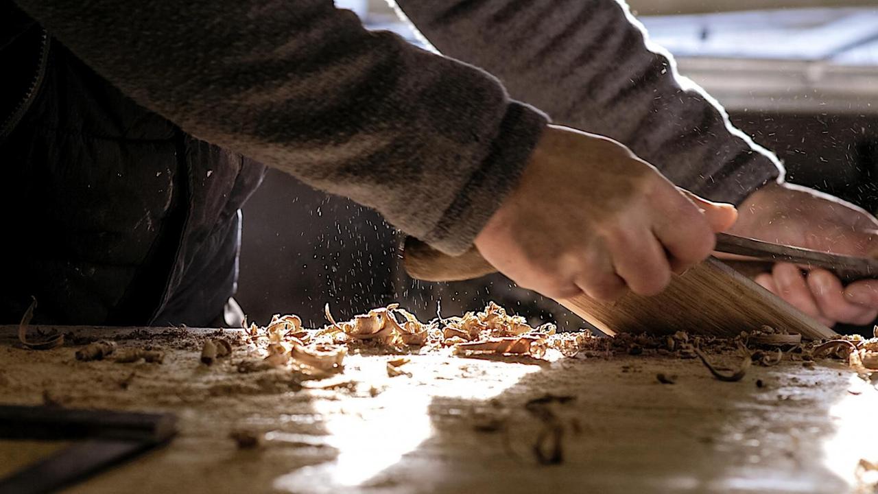 Eine Nahaufnahme von Tischlerhänden an der Hobelbank, die Holzspäne fliegen durch die Luft. Eine Nahaufnahme von Tischlerhänden an der Hobelbank, die Holzspäne fliegen durch die Luft.