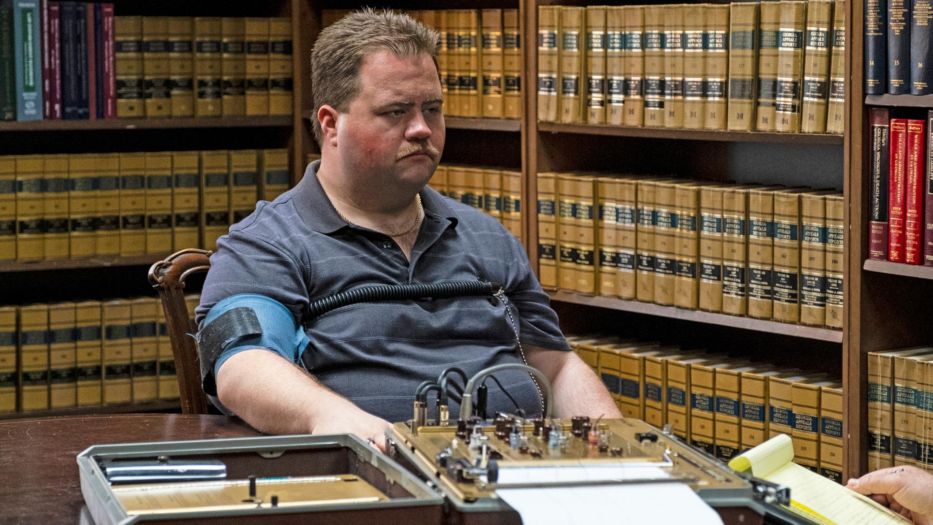 Paul Walter Hauser als Richard Jewell in "Der Fall Richard Jewell" sitzt an einem Schreibtisch während einer Befragung am Lügendetektor. Paul Walter Hauser als Richard Jewell in "Der Fall Richard Jewell" sitzt an einem Schreibtisch während einer Befragung am Lügendetektor.