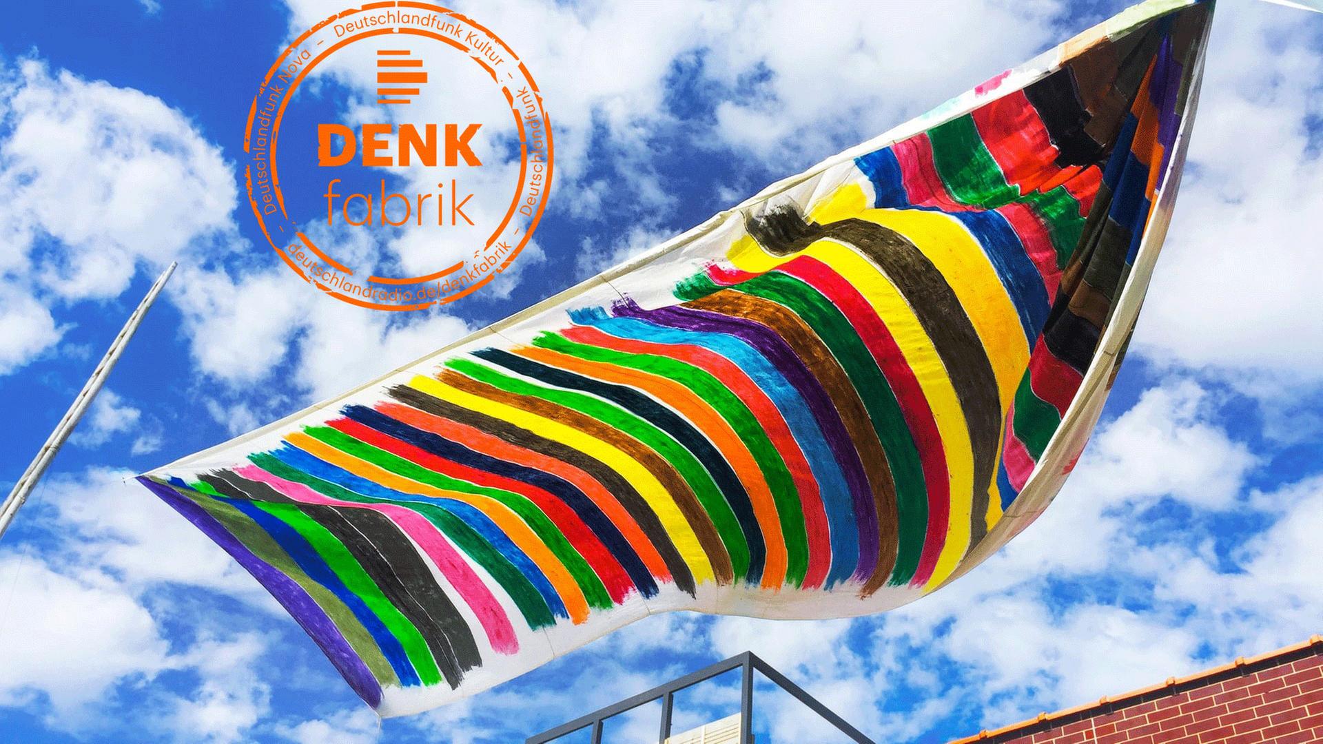 Vor einem blauen Himmel sieht man eine handgefertigte, handbemalte bunte Flagge wehen. Vor einem blauen Himmel sieht man eine handgefertigte, handbemalte bunte Flagge wehen.