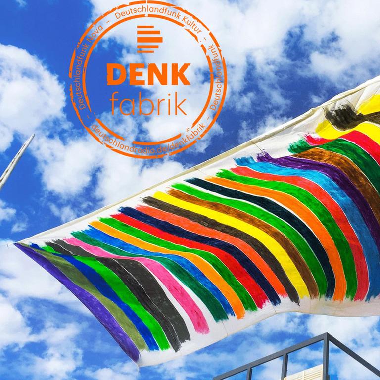 Vor einem blauen Himmel sieht man eine handgefertigte, handbemalte bunte Flagge wehen.