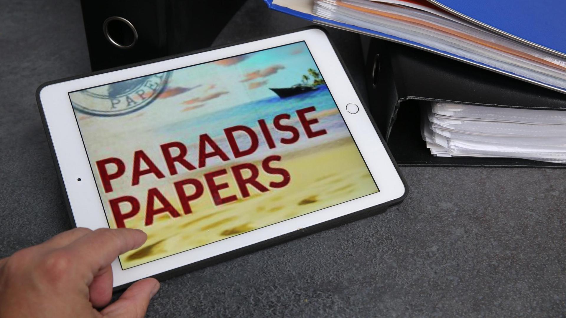 Eine Hand auf einem Tablet - auf dem Dislplay steht "Paradise Papers"