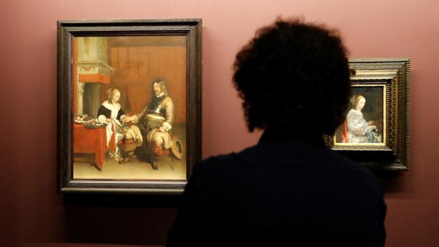 Man sieht die Silhouette eines Mannes, der sich im Pariser Louvre ein Gemälde von Gerard ter Borch anschaut.
