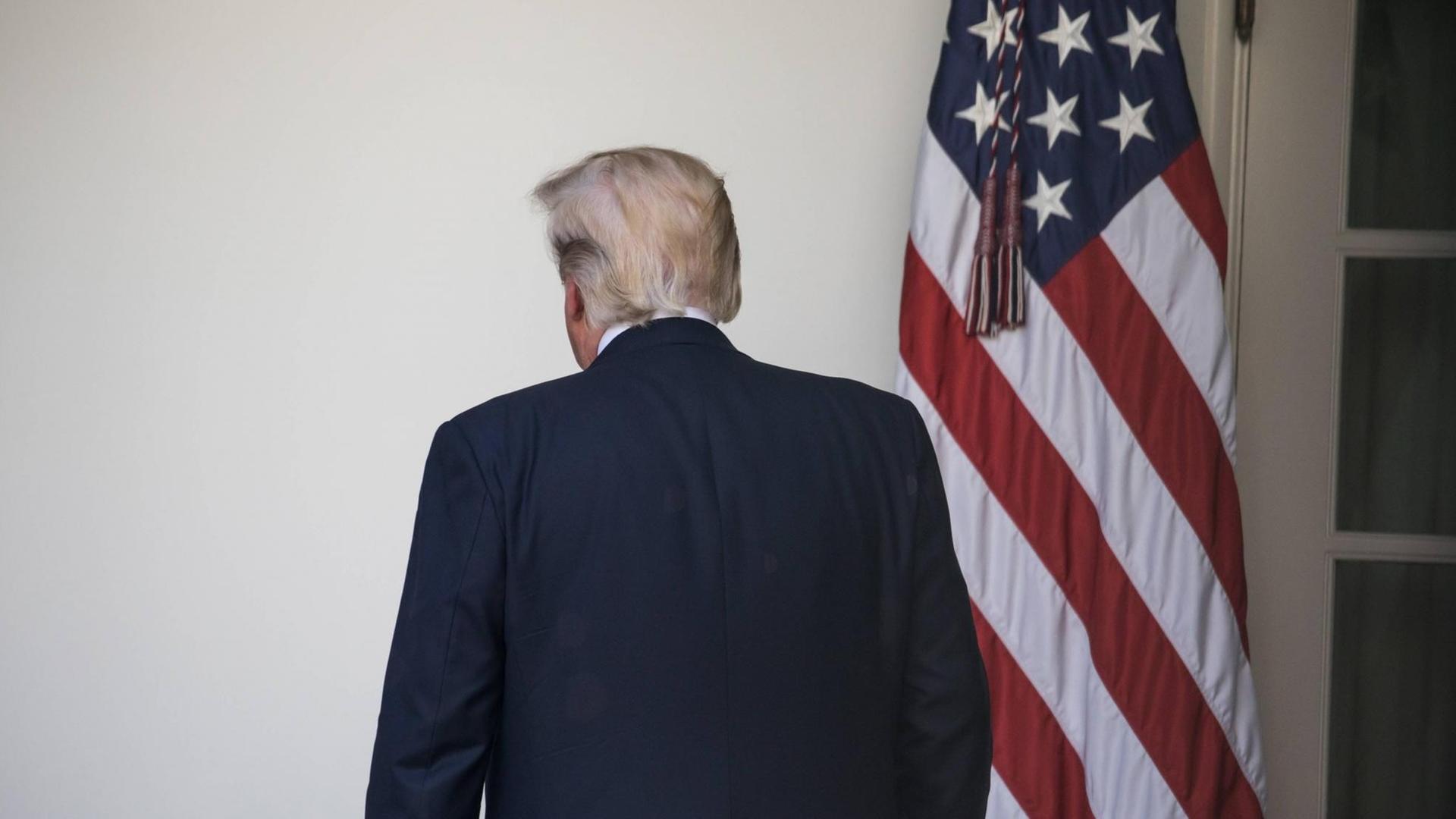 Präsident Trump wendet sich von der Kamera ab und geht Richtung Oval Office, rechts die US-Fahne.