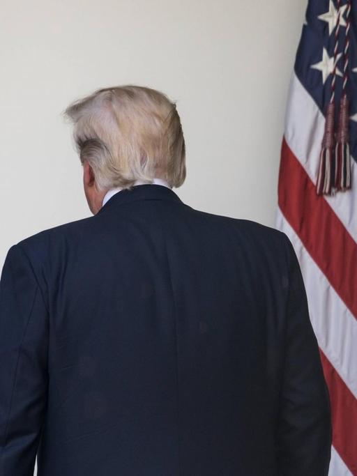 Präsident Trump wendet sich von der Kamera ab und geht Richtung Oval Office, rechts die US-Fahne.