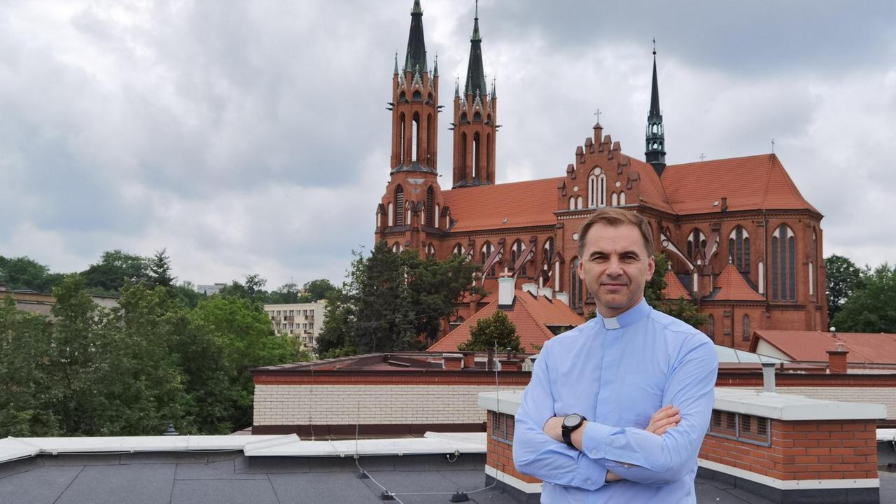Ein Mann im blauen Hemd mit Stehkragen steht mit verschränkten Armen von der Kathedrale in Bialystok. Ein Mann im blauen Hemd mit Stehkragen steht mit verschränkten Armen von der Kathedrale in Bialystok.