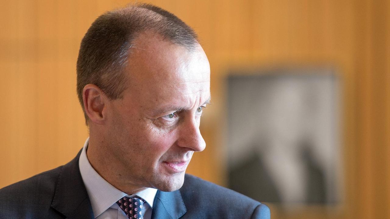 Merz' Gesicht wird vom Tageslicht auf der linken Hälfte hell angestrahlt. Hinter ihm sieht man eine braune Wand. Merz' Gesicht wird vom Tageslicht auf der linken Hälfte hell angestrahlt. Hinter ihm sieht man eine braune Wand.