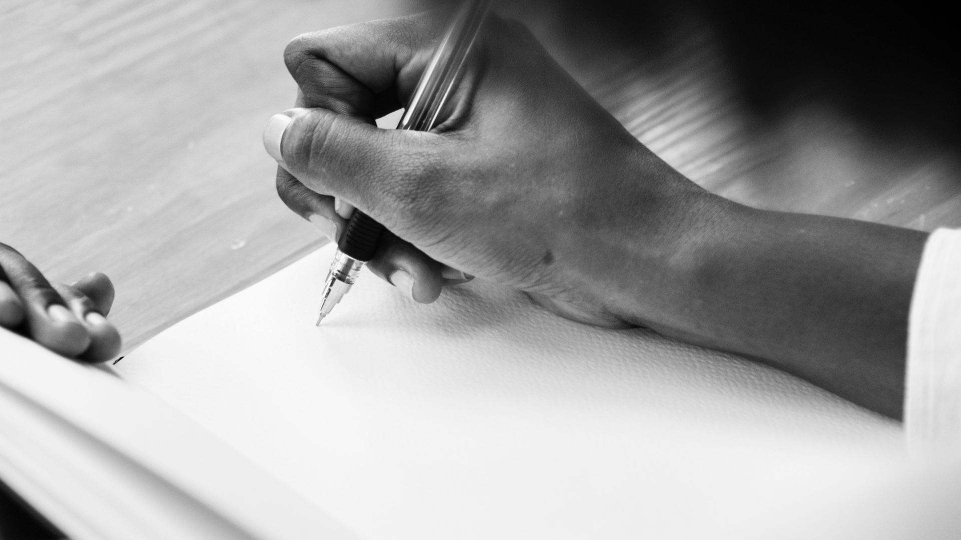 Eine Männerhand ist zu sehen, die einen Stift hält und dabei ist, etwas in einem leeren Buch zu notieren. Eine Männerhand ist zu sehen, die einen Stift hält und dabei ist, etwas in einem leeren Buch zu notieren.