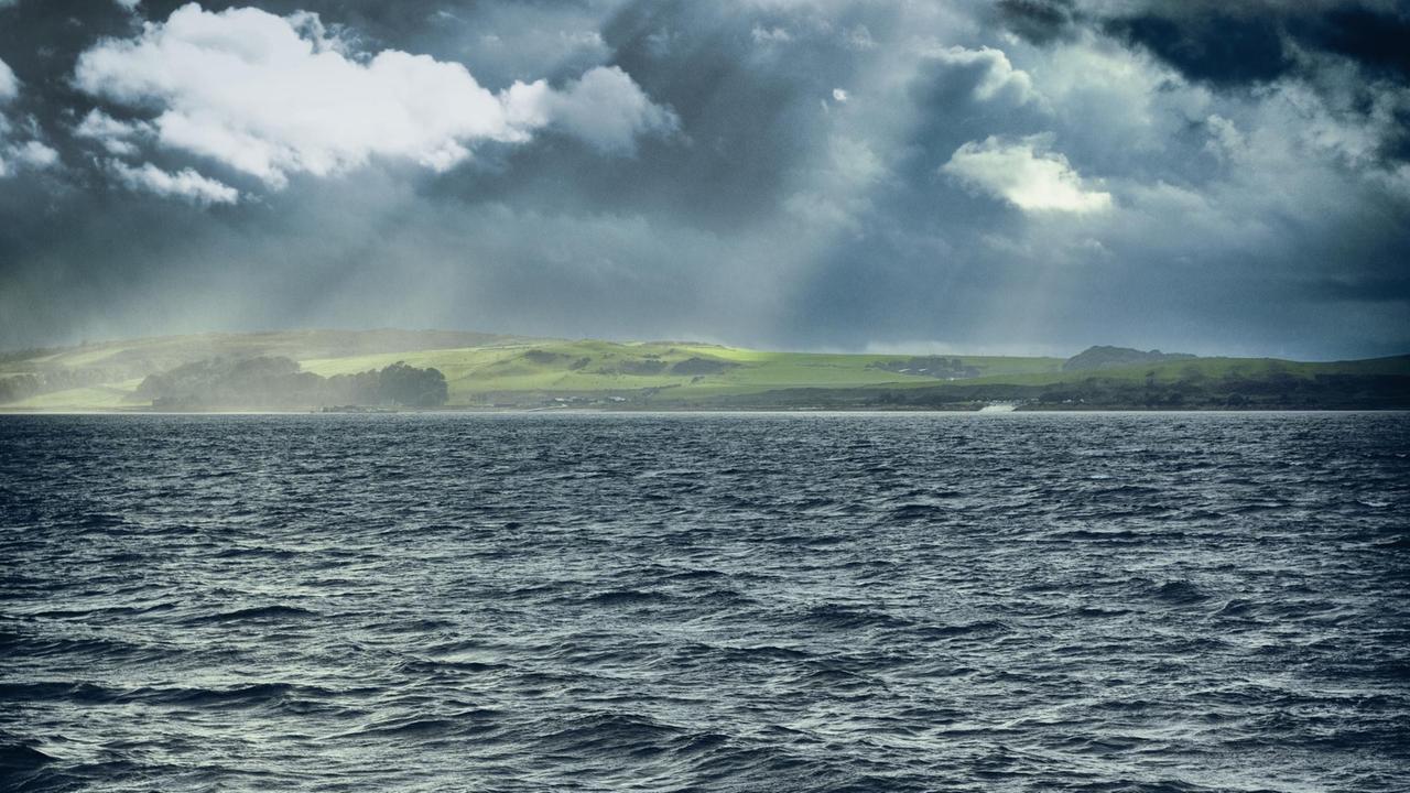 Unruhige See im Vordergrund, hinten eine Insel mit dunklen Wolken.
