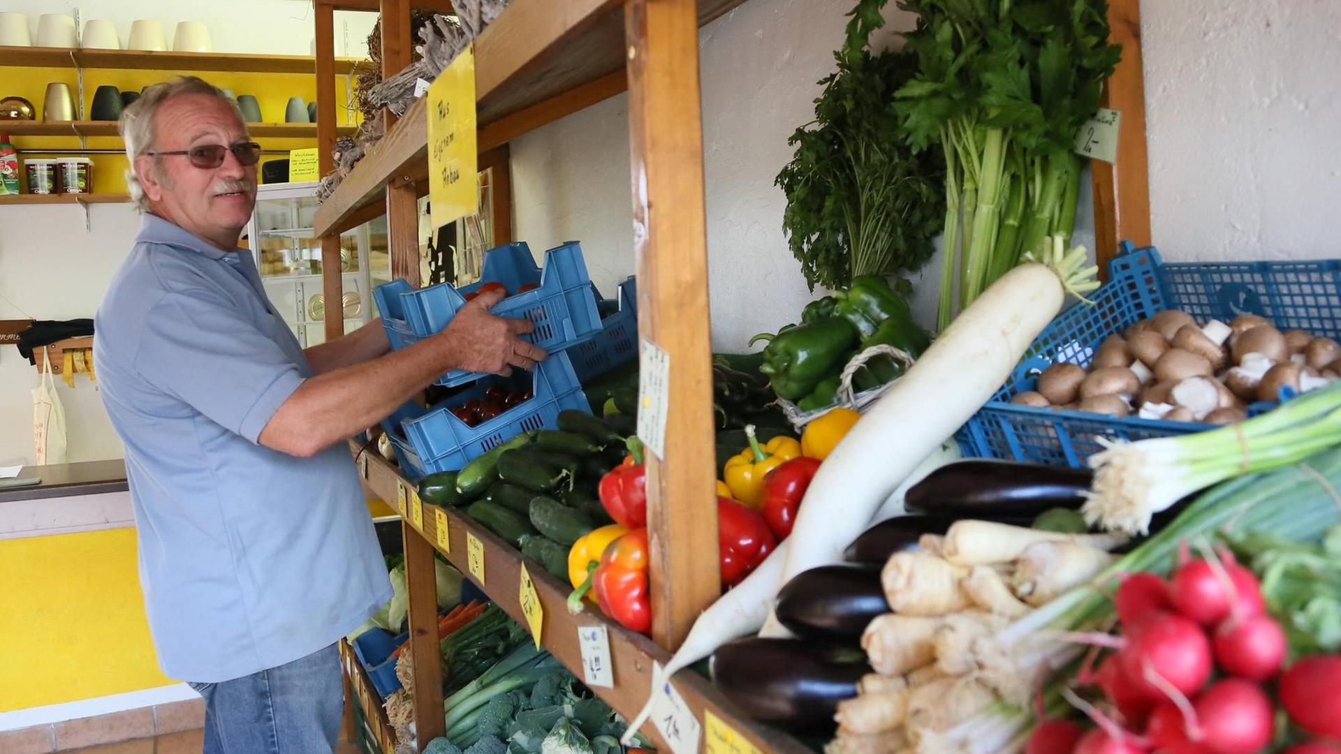 Ein Landwirt räumt Obst und Gemüse aus eigenem Anbau im Hofladen ein. Ein Landwirt räumt Obst und Gemüse aus eigenem Anbau im Hofladen ein.
