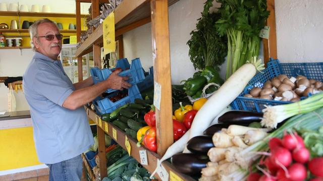 Ein Landwirt räumt Obst und Gemüse aus eigenem Anbau im Hofladen ein.