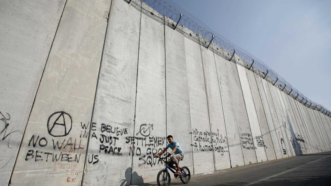 Ein arabischer Junge fährt im arabischen Teil in Ost-Jerusalem an der Mauer entlang, die den israelischen vom palästinensischen Teil trennt. Ein arabischer Junge fährt im arabischen Teil in Ost-Jerusalem an der Mauer entlang, die den israelischen vom palästinensischen Teil trennt.