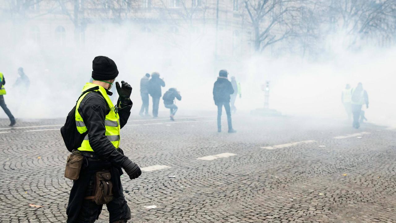Ein Mann während der Gelbwesten-Proteste in Paris schaut auf eine Straße, über die Rauch zieht