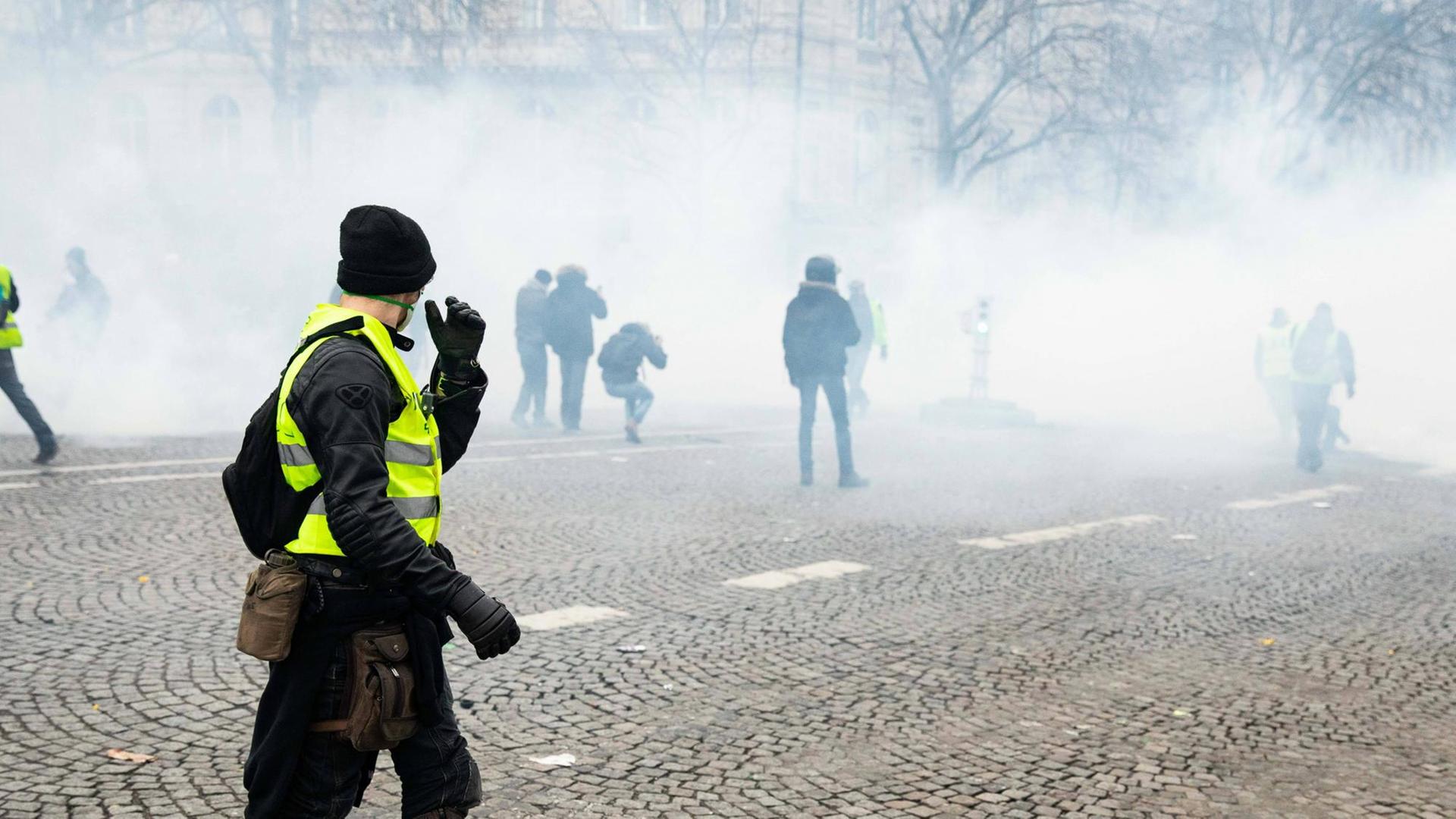 Ein Mann, der eine gelbe Weste trägt, schaut auf eine Straße, über die Rauch zieht Ein Mann, der eine gelbe Weste trägt, schaut auf eine Straße, über die Rauch zieht