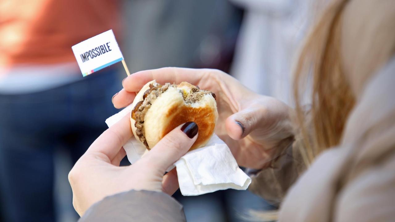Eine Frau hält einen Burger in den Händen. Darin steckt ein kleines Fähnchen mit der auuschrift "Impossible".