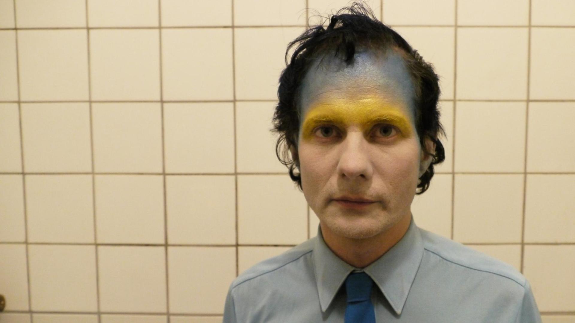 Felix Kubin, im Bad fotografiert, im Gesicht goldene und blaue Farbe.