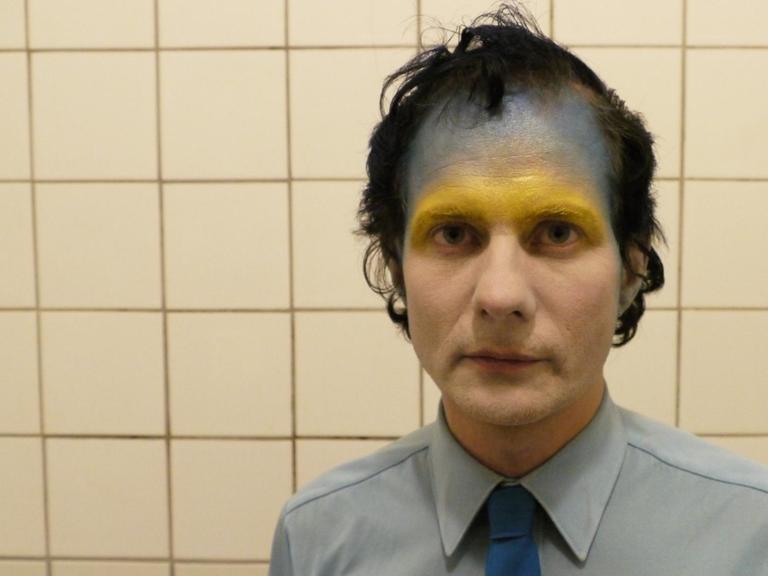 Felix Kubin, im Bad fotografiert, im Gesicht goldene und blaue Farbe.