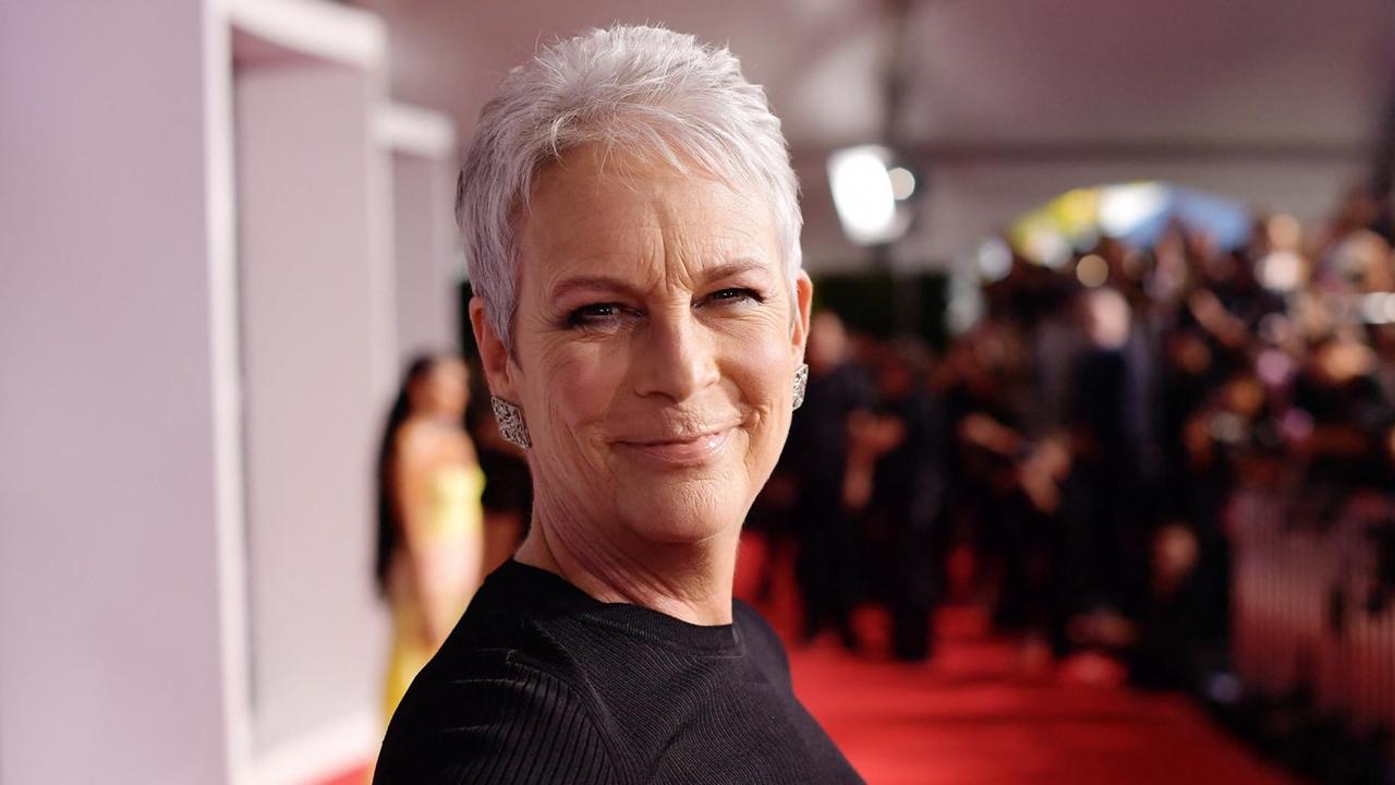 Jamie Lee Curtis steht auf einem Roten Teppich und lacht in die Kamera. Jamie Lee Curtis steht auf einem Roten Teppich und lacht in die Kamera.