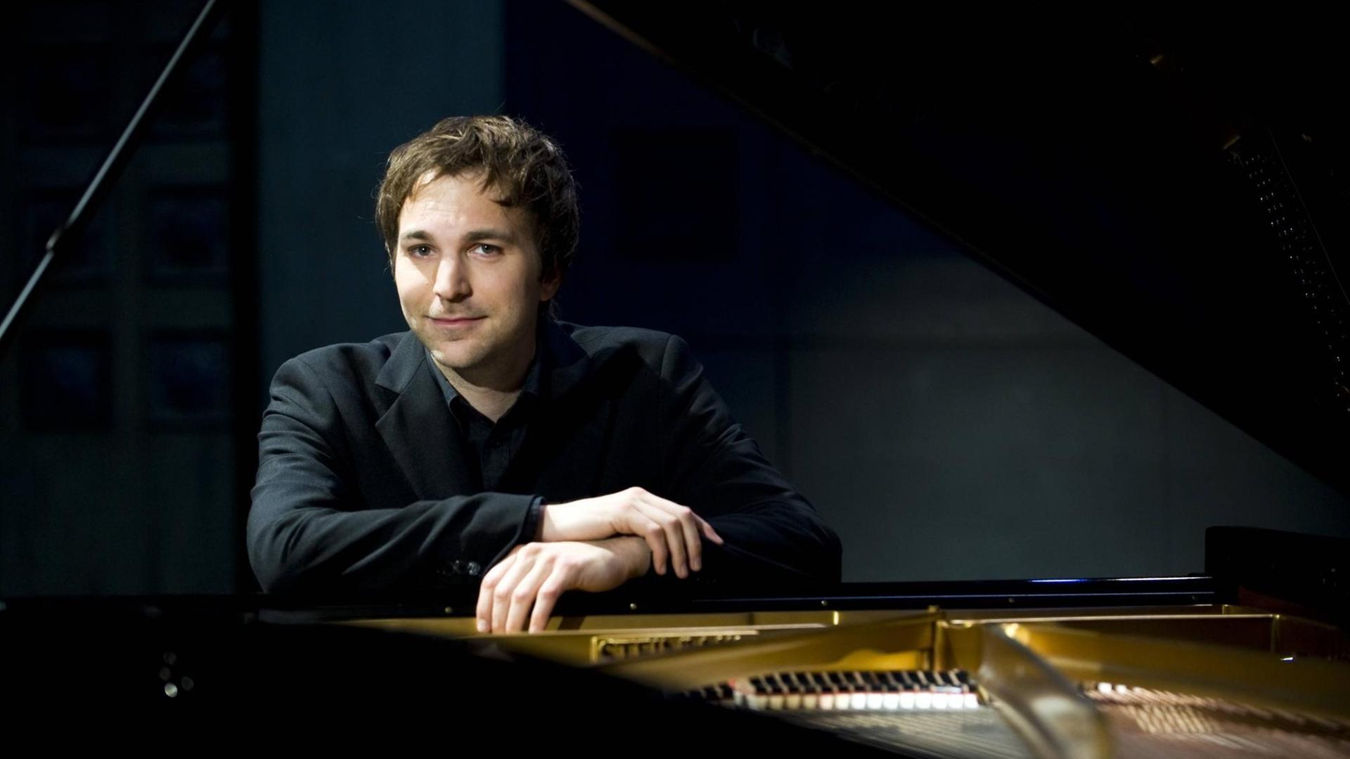 Portrait des Pianisten Herbert Schuch, durch einen geöffneten, schwarzen Konzertflügel hinweg fotografiert. Portrait des Pianisten Herbert Schuch, durch einen geöffneten, schwarzen Konzertflügel hinweg fotografiert.