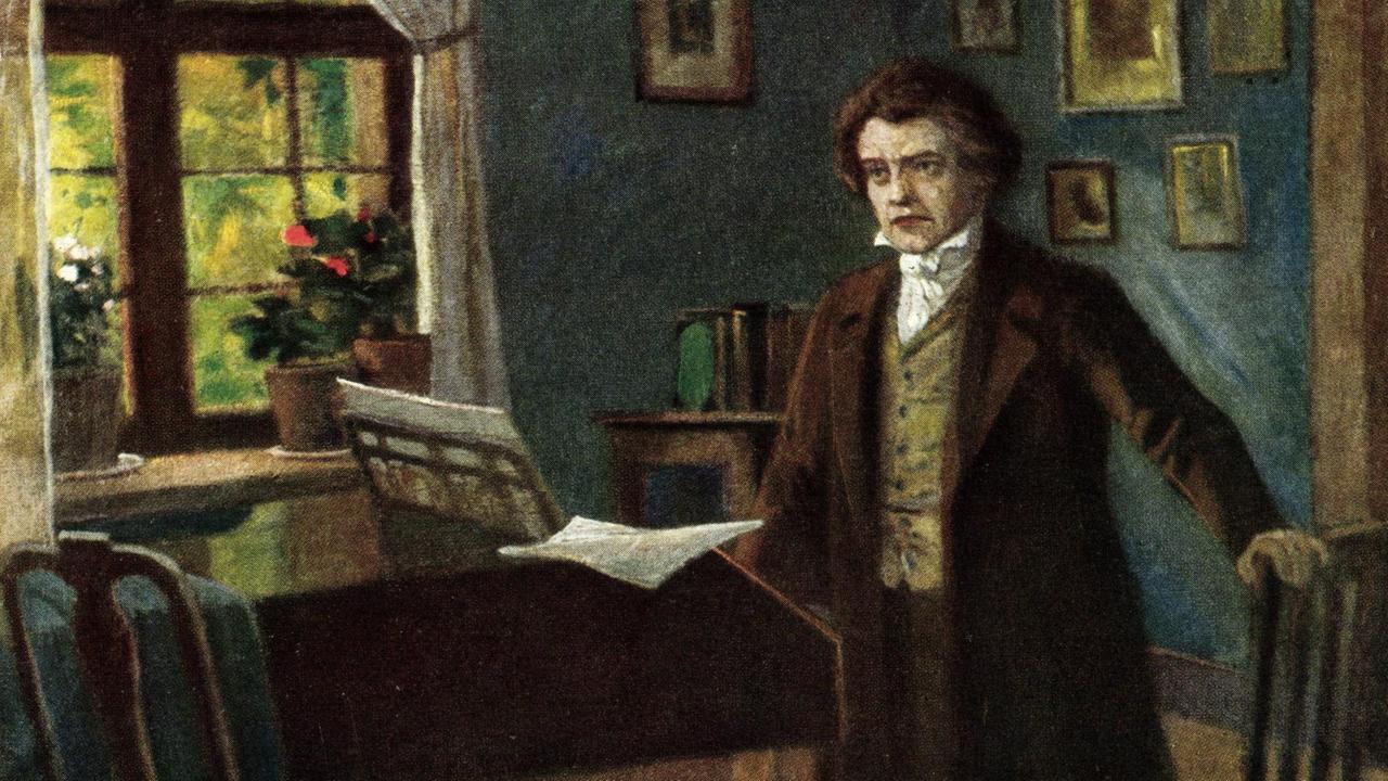 Ludwig van Beethoven steht in einem Zimmer mit einem Flügel im Hintergrund.