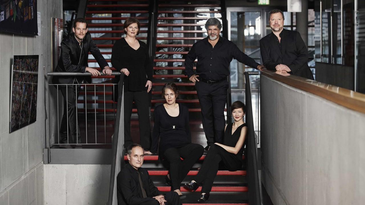 Die sieben Sänger und Sängerinnen haben sich in einem von Beton dominierten Treppenhaus gruppiert. Die sieben Sänger und Sängerinnen haben sich in einem von Beton dominierten Treppenhaus gruppiert.