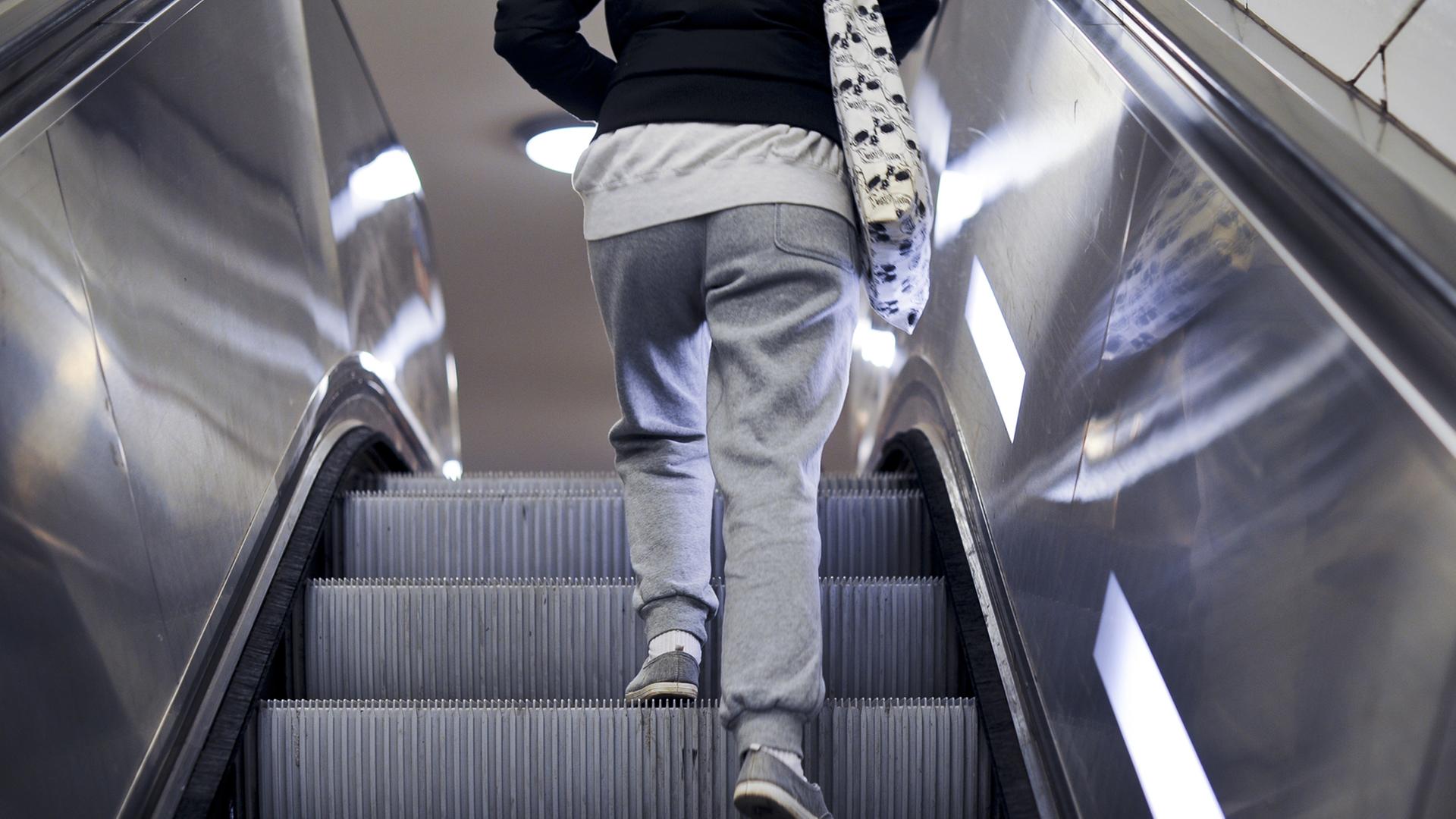 Eine Frau in Jogginghose steht auf einer Rolltreppe. Eine Frau in Jogginghose steht auf einer Rolltreppe.