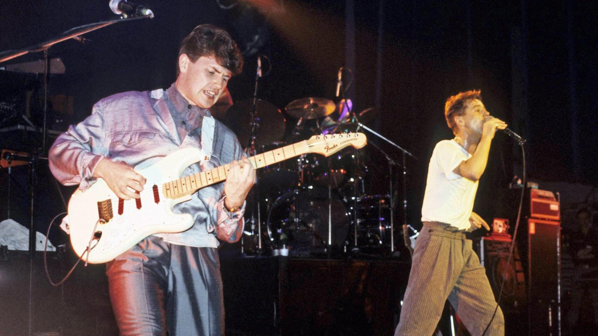 Gitarrist Charlie Burchill und Sänger Jim Kerr von den Simple Minds stehen auf einer Kozertbühne. Gitarrist Charlie Burchill und Sänger Jim Kerr von den Simple Minds stehen auf einer Kozertbühne.