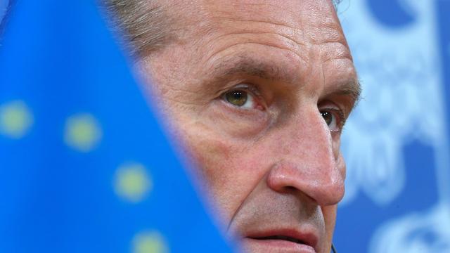 Der EU-Kommissar für Digitale Wirtschaft, Günther Oettinger, mit ernstem Blick. Sein Gesicht wird halb verdeckt von einer Europa-Flagge. 