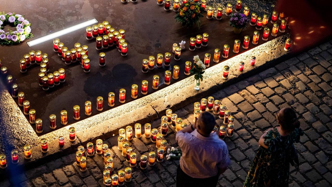 Ein Mann und eine Frau stehen vor brennenden Kerzen in Form der Jahreszahl "2010" und dem Unglücksdatum "24.7." an der Unglücksstelle der Loveparade 2010. Mit brennenden Kerzen wurde in Duisburg der Opfer der Loveparade-Katastrophe vor neun Jahren gedacht.