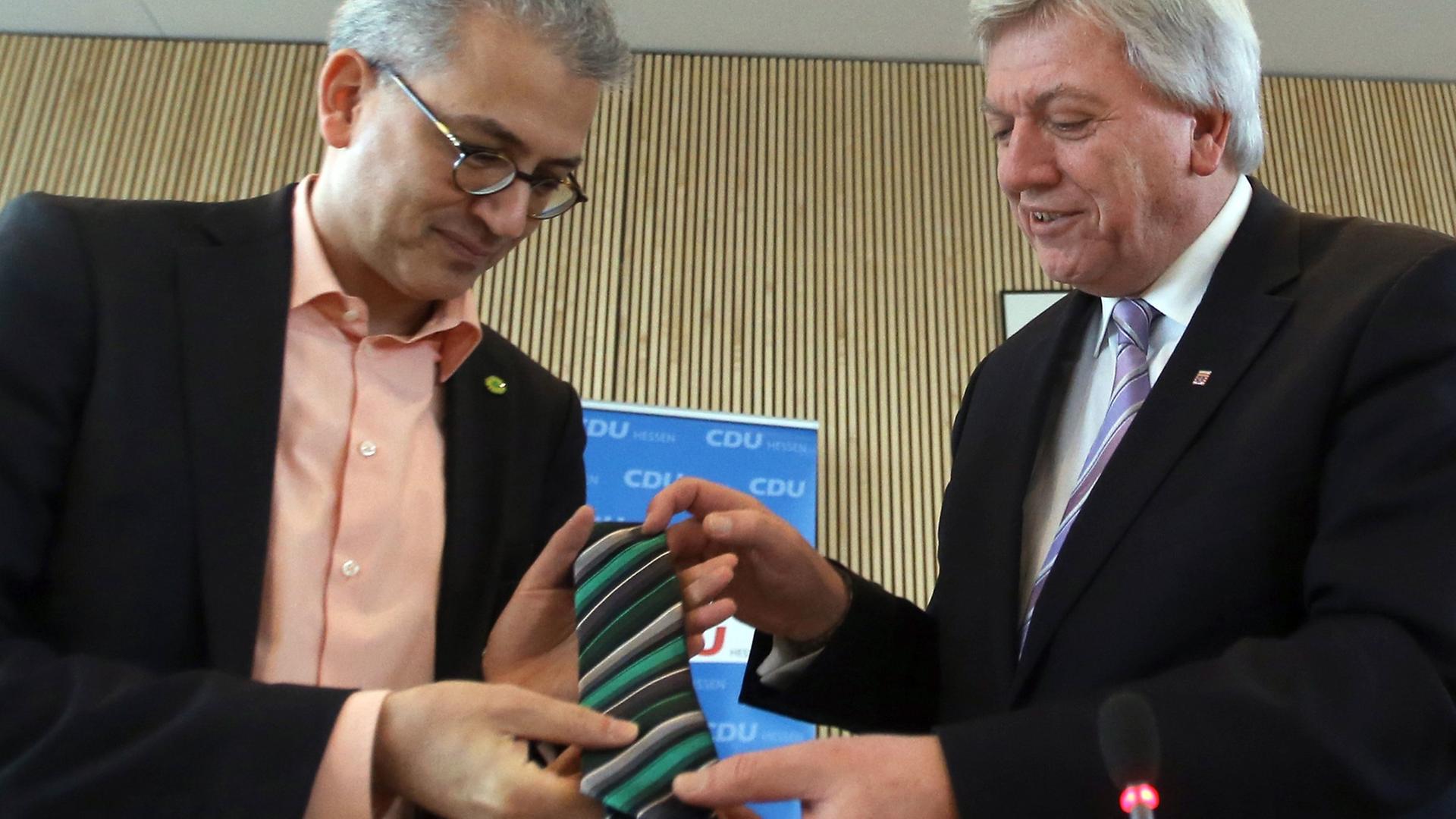Der Ministerpräsident von Hessen, Volker Bouffier (CDU, r), überreicht dem Vorsitzenden von Bündnis 90/Die Grünen in Hessen, Tarek Al-Wazir (l), eine schwarz-grüne Krawatte. Der Ministerpräsident von Hessen, Volker Bouffier (CDU, r), überreicht dem Vorsitzenden von Bündnis 90/Die Grünen in Hessen, Tarek Al-Wazir (l), eine schwarz-grüne Krawatte.