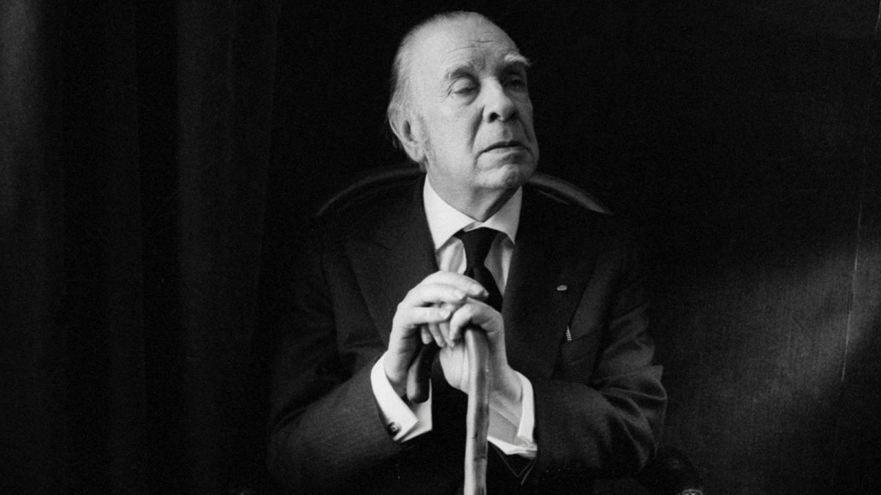 Porträt von Jorge Luis Borges, der in einem Sessel sitzt und sich auf seinen Spazierstock stützt.