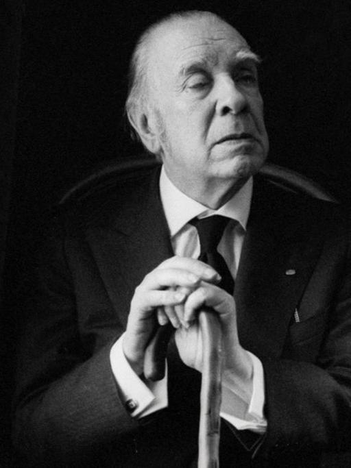 Porträt von Jorge Luis Borges, der in einem Sessel sitzt und sich auf seinen Spazierstock stützt.