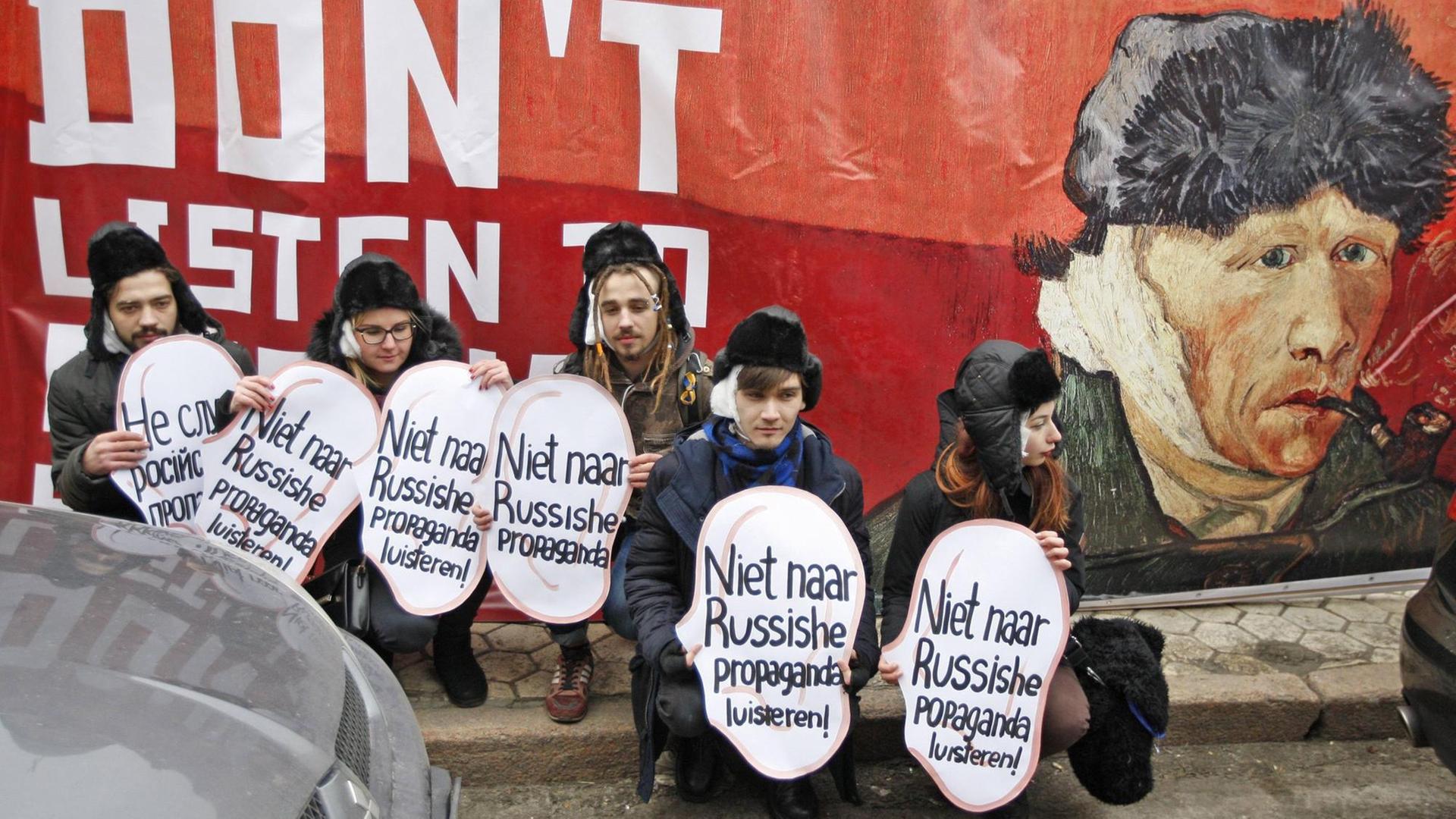 Ukrainische Aktivisten halten vor einem Porträt des niederländischen Malers Vincent van Gogh Plakate in Ohrform hoch mit der Aufschrift "Nicht auf russische Propaganda hören."