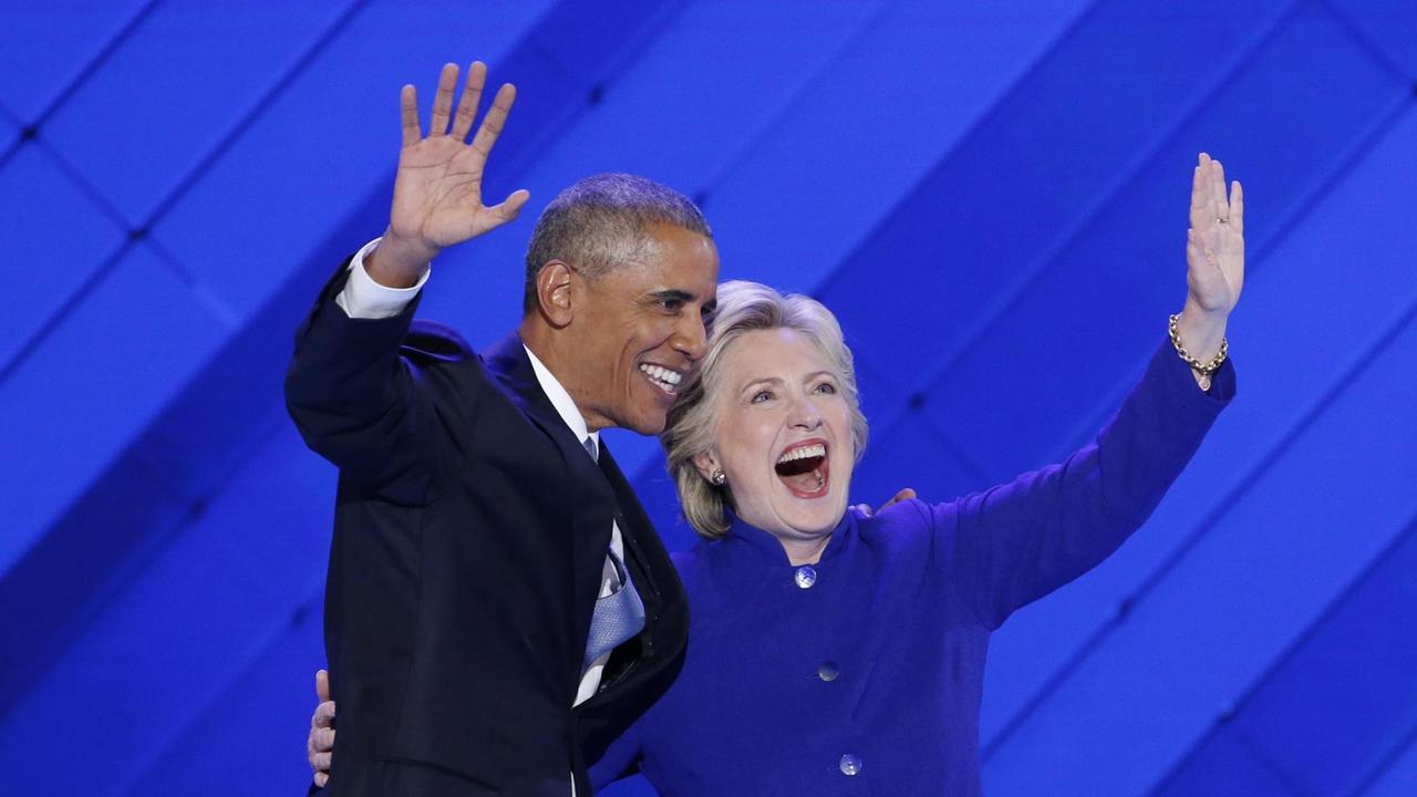 2016: US-Präsident Barack Obama und Präsidentschaftsbewerberin Hillary Clinton umarmen sich auf dem Parteitag der US-Demokraten und winken den Delegierten zu.