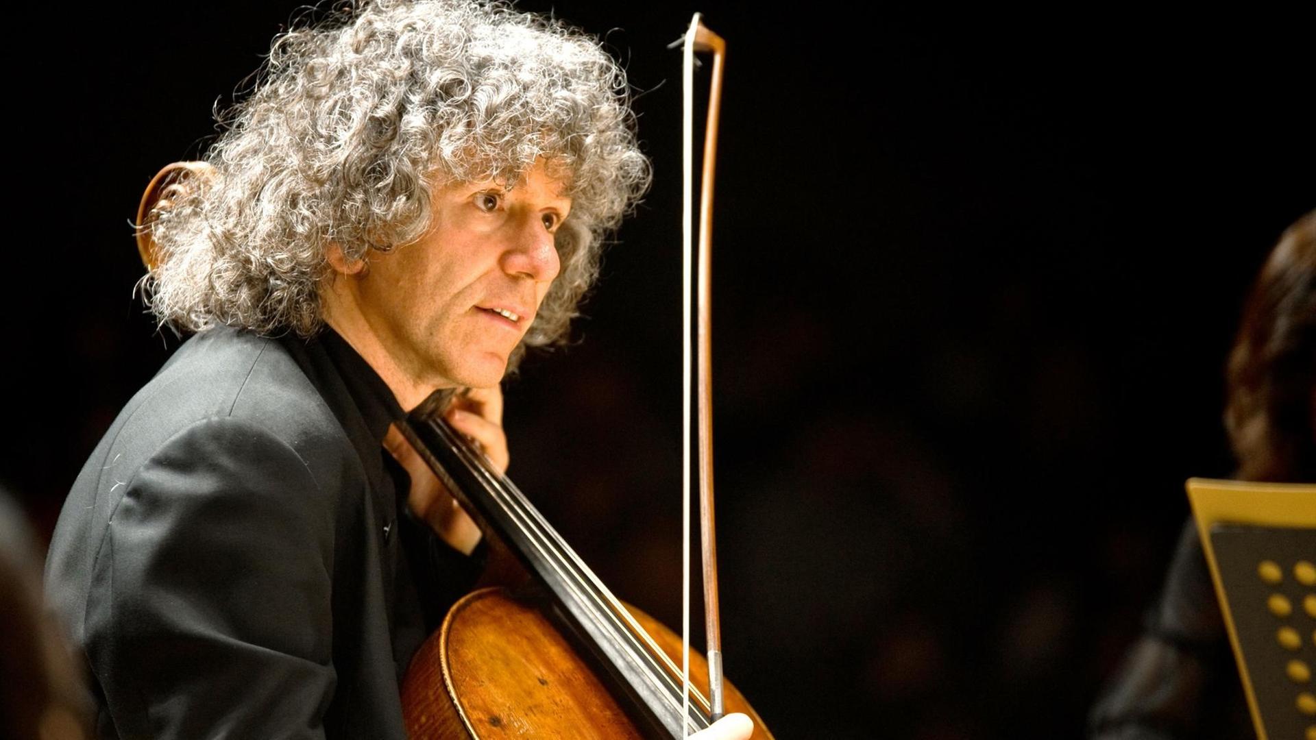 Ein Mann mit weiß-grauen Locken in der Halbtotalen: Er hält vor sich ein holzfarbenes Cello und in der rechten Hand den Bogen. Ein Mann mit weiß-grauen Locken in der Halbtotalen: Er hält vor sich ein holzfarbenes Cello und in der rechten Hand den Bogen.