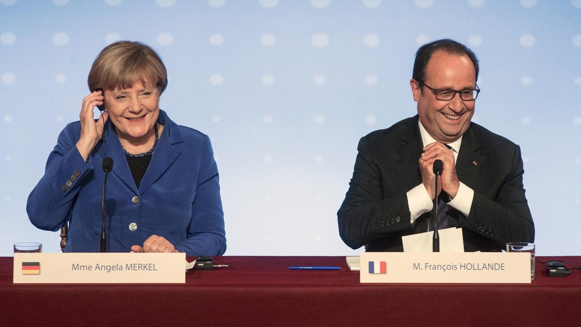 Bundeskanzlerin Angela Merkel und Frankreichs Präsident Francois Hollande geben nach dem Ukraine-Gipfel eine Pressekonferenz. Sie sitzen hinter einem Pult und grinsen. Bundeskanzlerin Angela Merkel und Frankreichs Präsident Francois Hollande geben nach dem Ukraine-Gipfel eine Pressekonferenz. Sie sitzen hinter einem Pult und grinsen.